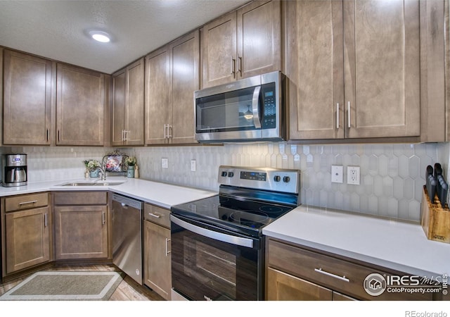 kitchen with appliances with stainless steel finishes, a textured ceiling, backsplash, and sink