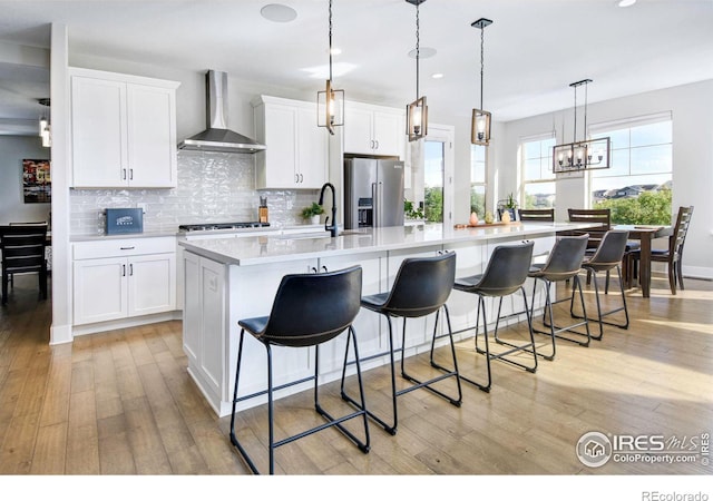 kitchen with wall chimney exhaust hood, high end fridge, hanging light fixtures, a large island, and white cabinets