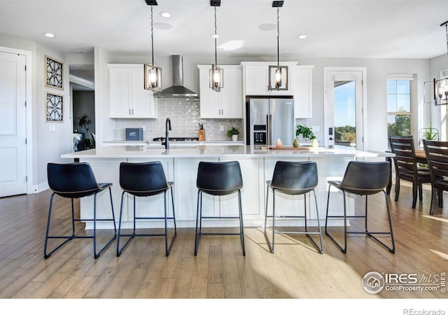 kitchen featuring pendant lighting, white cabinetry, a spacious island, high end refrigerator, and wall chimney exhaust hood