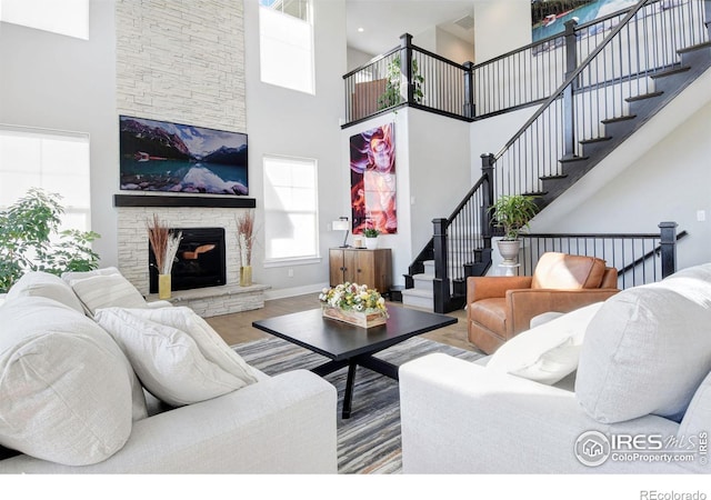 living room featuring a towering ceiling, wood-type flooring, and a stone fireplace