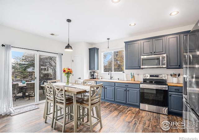 kitchen featuring butcher block counters, dark hardwood / wood-style flooring, pendant lighting, and appliances with stainless steel finishes