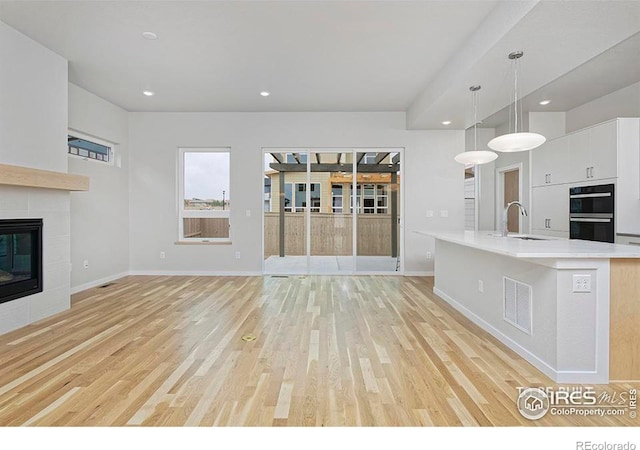 kitchen with a fireplace, sink, hanging light fixtures, and light wood-type flooring