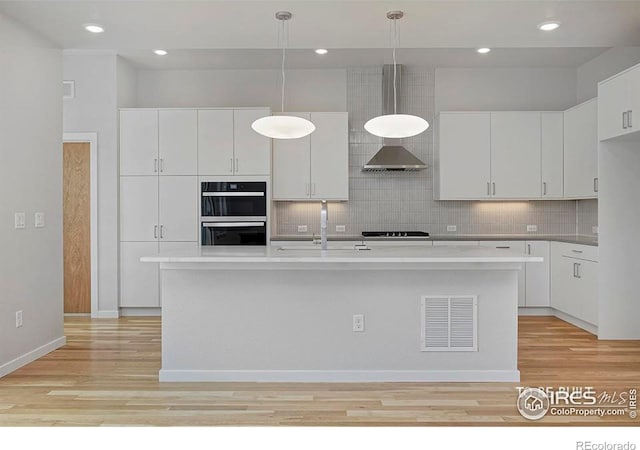 kitchen with white cabinetry, a center island with sink, and pendant lighting