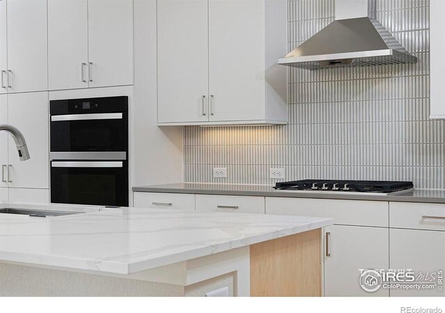 kitchen with wall chimney exhaust hood, stainless steel appliances, light stone counters, decorative backsplash, and white cabinets