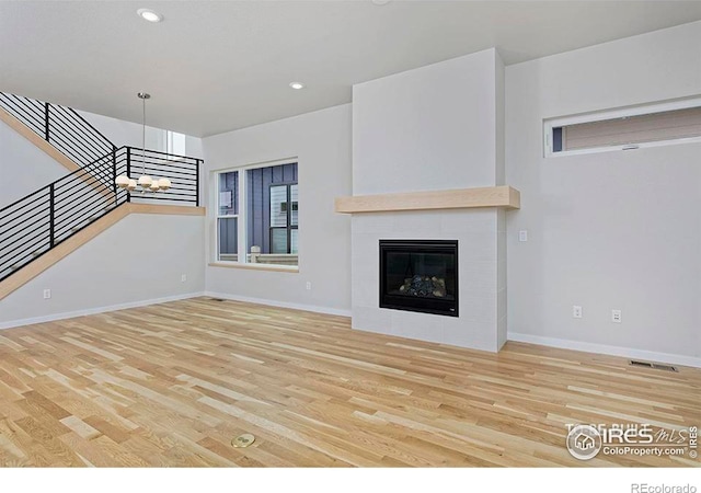 unfurnished living room with a fireplace, an inviting chandelier, and light hardwood / wood-style flooring