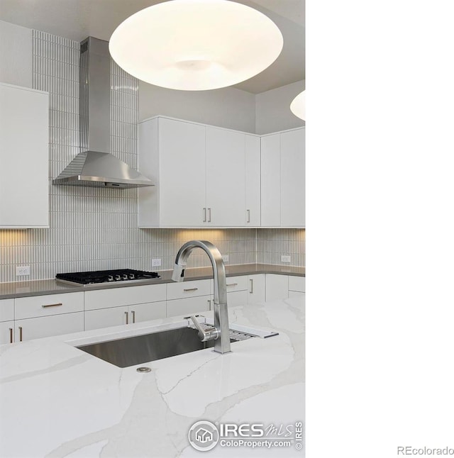 kitchen with gas cooktop, light stone countertops, wall chimney exhaust hood, sink, and white cabinetry