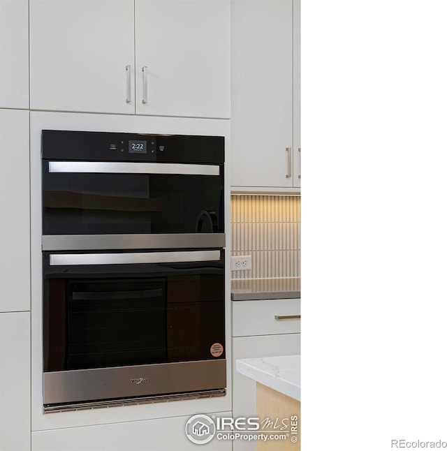 kitchen with white cabinetry, light stone countertops, and stainless steel double oven