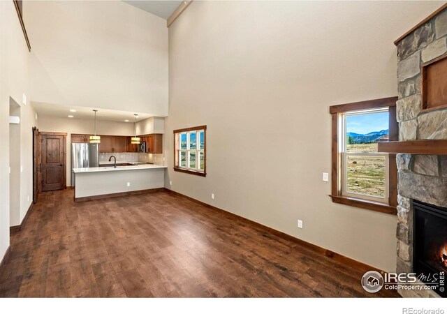 unfurnished living room with a fireplace, a towering ceiling, dark hardwood / wood-style floors, and sink