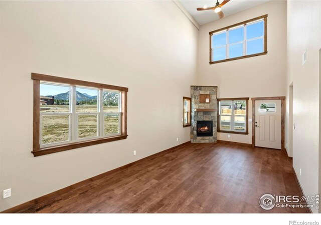 unfurnished living room with a mountain view, a towering ceiling, dark hardwood / wood-style floors, and a stone fireplace