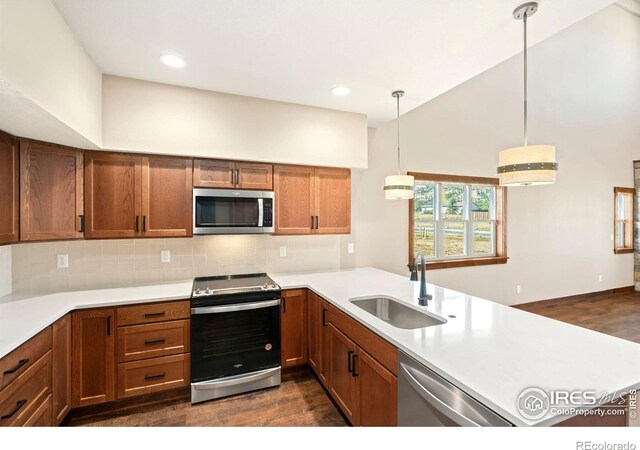 kitchen with pendant lighting, dark wood-type flooring, sink, appliances with stainless steel finishes, and kitchen peninsula