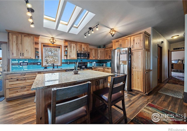 kitchen featuring a skylight, dark hardwood / wood-style floors, light stone countertops, appliances with stainless steel finishes, and a kitchen island