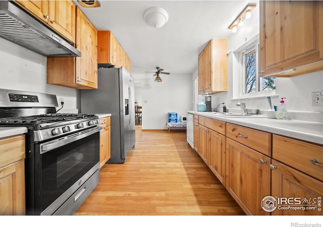 kitchen with appliances with stainless steel finishes, ceiling fan, sink, exhaust hood, and light hardwood / wood-style floors