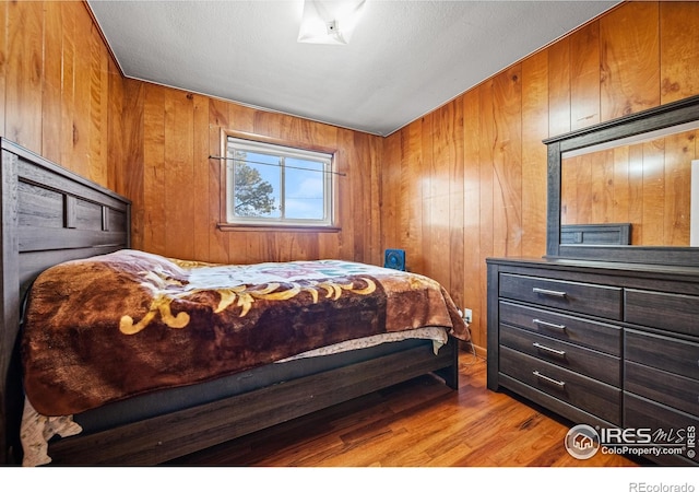 bedroom with a textured ceiling, wooden walls, and light hardwood / wood-style flooring