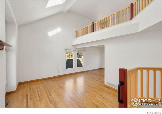 unfurnished living room featuring a skylight, beam ceiling, high vaulted ceiling, and light hardwood / wood-style flooring