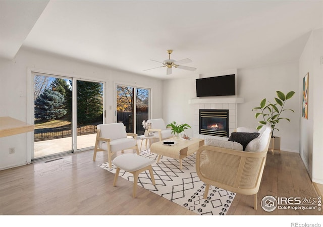 living room featuring a tile fireplace, hardwood / wood-style floors, and ceiling fan