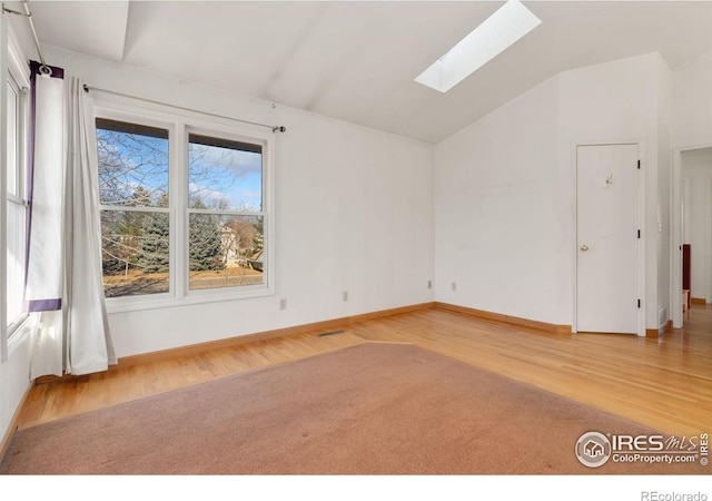 spare room with light hardwood / wood-style flooring, vaulted ceiling with skylight, and a healthy amount of sunlight