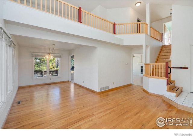 unfurnished living room featuring a notable chandelier, light hardwood / wood-style floors, and a high ceiling