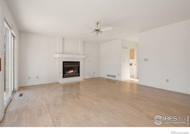 unfurnished living room with ceiling fan, a tile fireplace, and light wood-type flooring