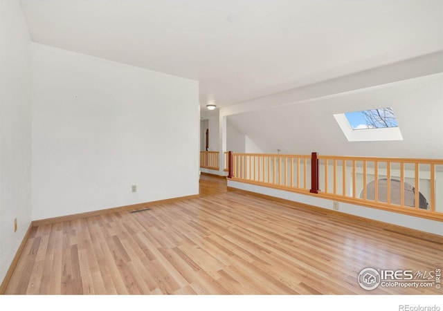 empty room featuring light hardwood / wood-style floors and vaulted ceiling with skylight