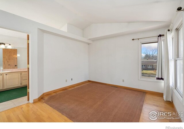 spare room with lofted ceiling, sink, and light hardwood / wood-style flooring