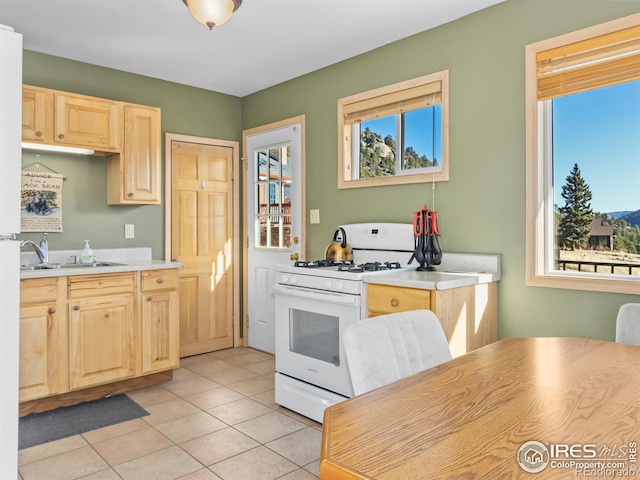 kitchen with sink, light brown cabinets, light tile patterned floors, and white gas range oven