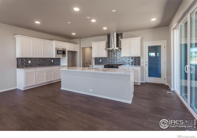 6105 Saddle Horn Dr, Timnath, CO 80547 - kitchen featuring stainless steel microwave, wall chimney range hood, backsplash, dark wood-type flooring, and an island with sink