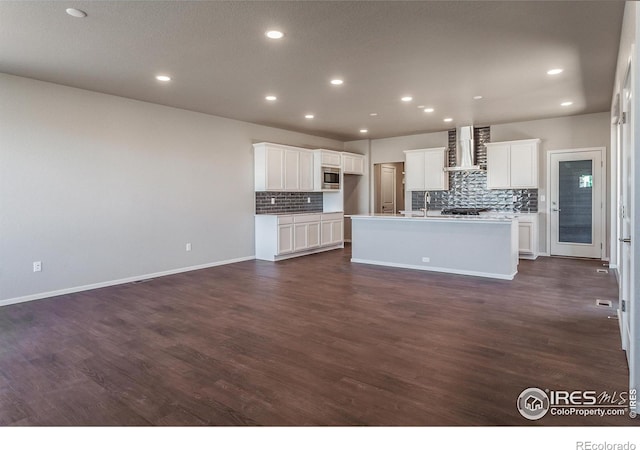 6105 Saddle Horn Dr, Timnath, CO 80547 - kitchen with wall chimney exhaust hood, stainless steel microwave, backsplash, a center island with sink, and dark wood-style flooring