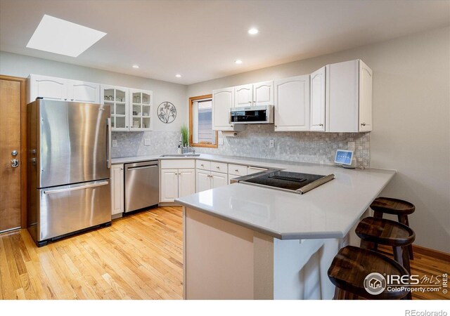 kitchen featuring a skylight, kitchen peninsula, white cabinets, and appliances with stainless steel finishes