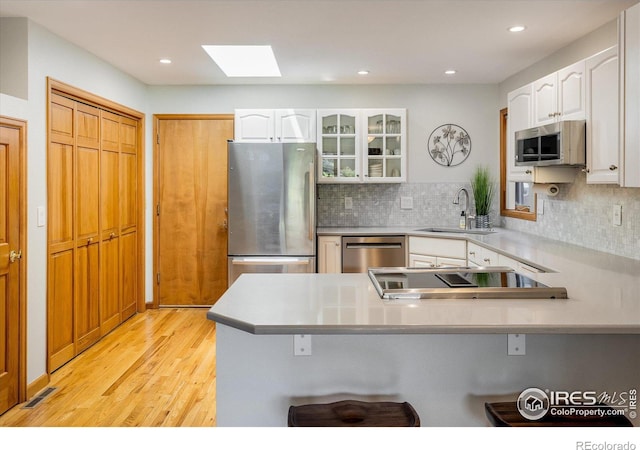 kitchen featuring kitchen peninsula, appliances with stainless steel finishes, light wood-type flooring, a skylight, and white cabinets