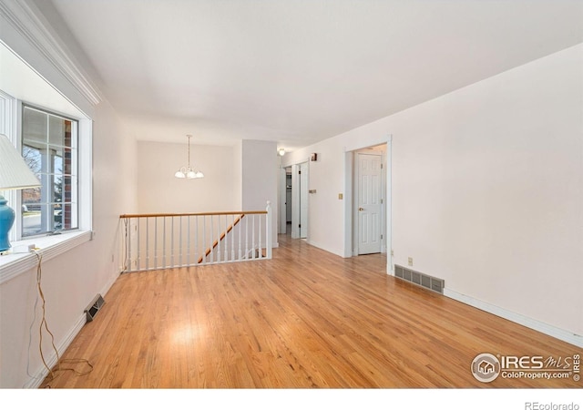 spare room with light hardwood / wood-style floors and a notable chandelier