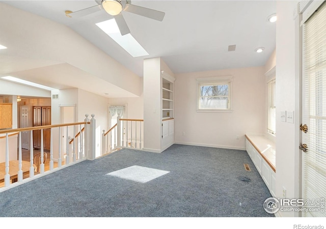 unfurnished room with dark colored carpet, built in shelves, lofted ceiling with skylight, and ceiling fan