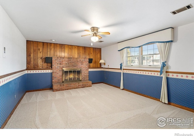 unfurnished living room featuring ceiling fan, wood walls, carpet floors, and a brick fireplace