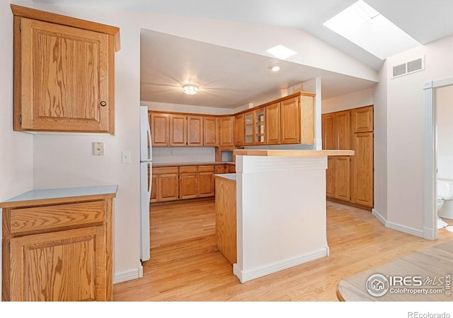 kitchen featuring kitchen peninsula, white refrigerator, light hardwood / wood-style flooring, and lofted ceiling with skylight