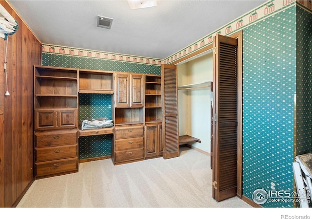 interior space featuring wooden walls, built in desk, light colored carpet, and a textured ceiling