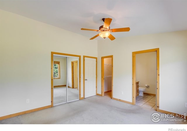 unfurnished bedroom featuring connected bathroom, ceiling fan, light colored carpet, and a walk in closet