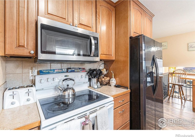 kitchen with appliances with stainless steel finishes, brown cabinetry, light countertops, and backsplash