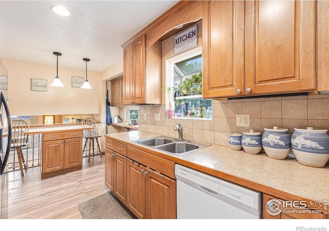 kitchen featuring tasteful backsplash, dishwasher, brown cabinets, decorative light fixtures, and a sink