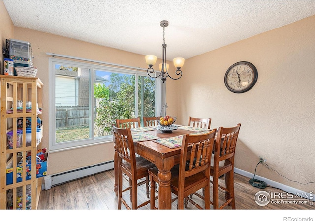 dining area with a notable chandelier, a textured wall, a baseboard heating unit, wood finished floors, and baseboards