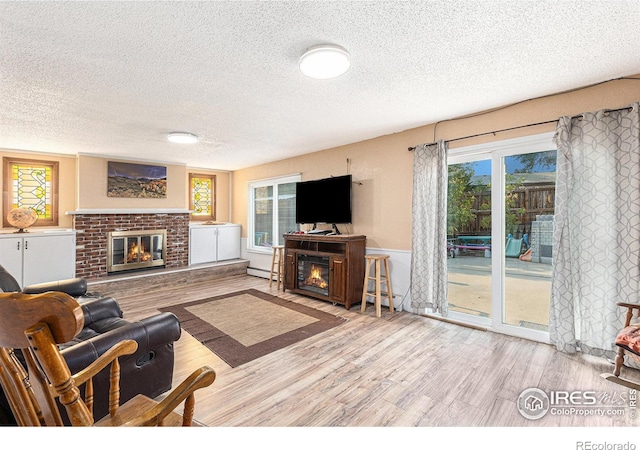 living room featuring a wealth of natural light, a brick fireplace, a textured ceiling, and wood finished floors