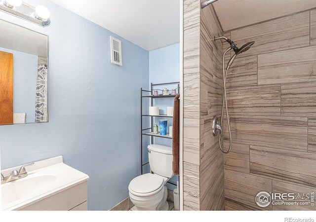 bathroom featuring visible vents, vanity, a tile shower, and toilet