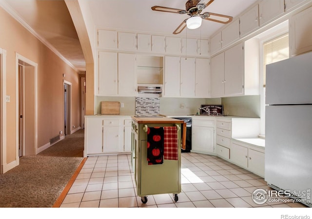 kitchen with ceiling fan, white cabinetry, white refrigerator, light tile patterned floors, and ornamental molding