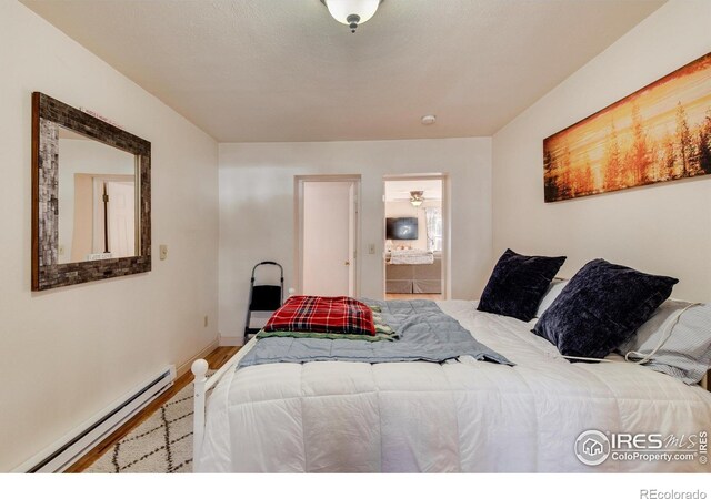 bedroom with ensuite bath, hardwood / wood-style floors, and a baseboard heating unit