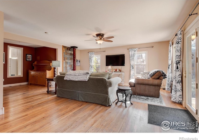 living room with a wood stove, ceiling fan, plenty of natural light, and light hardwood / wood-style floors