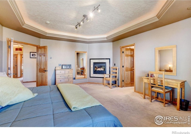 carpeted bedroom with a textured ceiling, rail lighting, a tile fireplace, and a tray ceiling