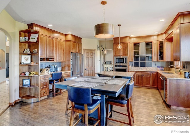 kitchen with decorative backsplash, appliances with stainless steel finishes, decorative light fixtures, a center island, and light hardwood / wood-style floors