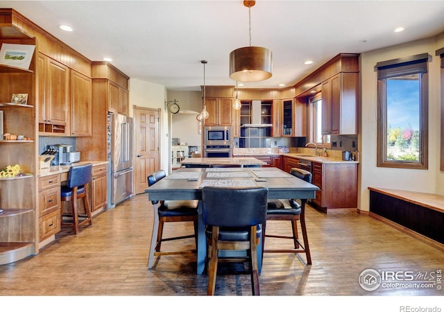 kitchen featuring appliances with stainless steel finishes, light wood-type flooring, decorative light fixtures, and a kitchen island