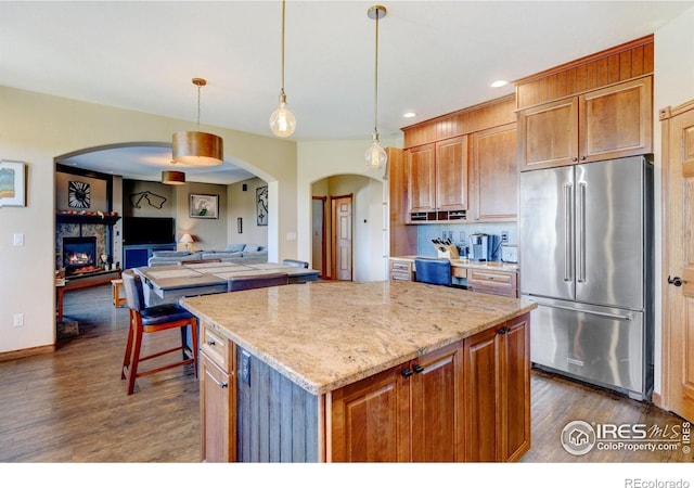 kitchen featuring dark wood-type flooring, high end refrigerator, a stone fireplace, hanging light fixtures, and a kitchen island