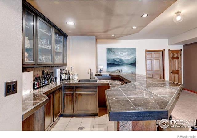 kitchen with kitchen peninsula, dark brown cabinetry, sink, and light tile patterned flooring