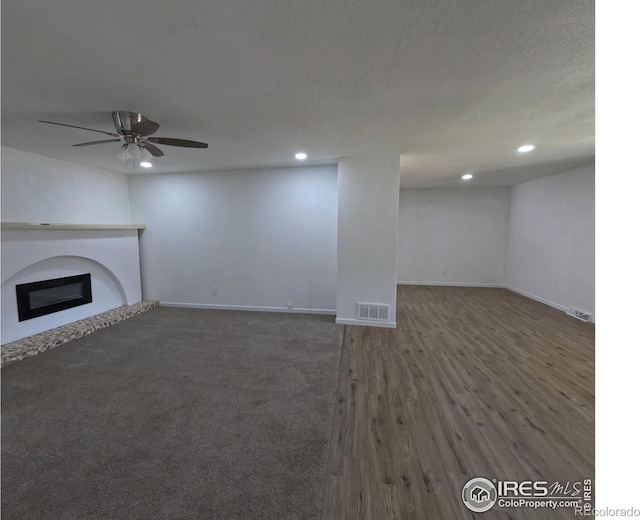 unfurnished living room featuring ceiling fan, dark hardwood / wood-style flooring, and a textured ceiling