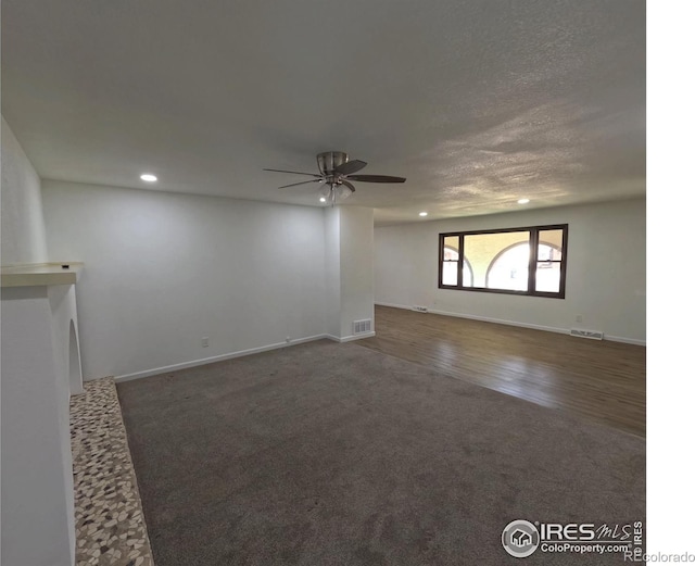 unfurnished living room with dark carpet, a textured ceiling, and ceiling fan